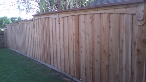 Vertical board-on-board wood fence construction featuring tightly fit planks and a capping trim piece across the top
