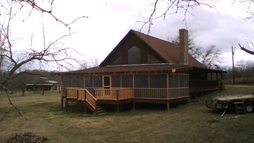 Screened porch attached to a house, featuring wooden railings and steps on an elevated deck